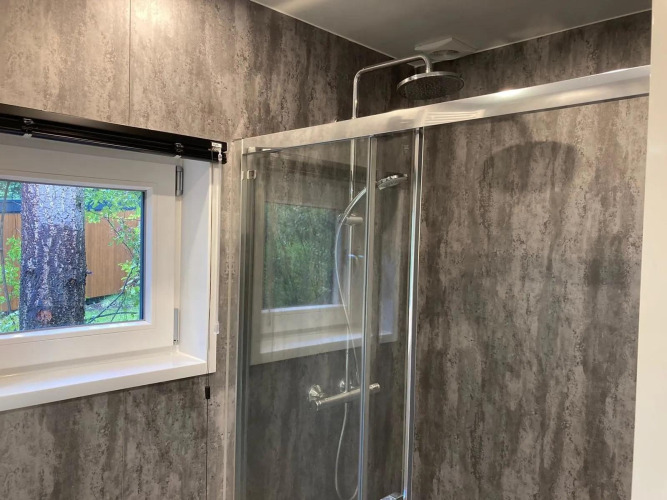 Badezimmer in einer Lodge mit grauen Wänden, Glasdusche und Fenster mit Blick auf einen Baum draußen.