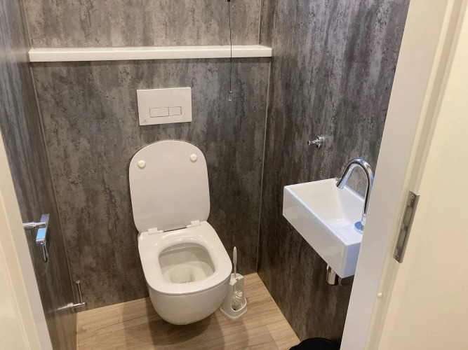 Kleines Badezimmer in einer Lodge mit wandhängender Toilette und kleinem Waschbecken an grauer Wand.