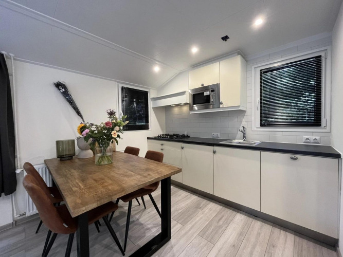 Modernes Glamping-Küche und Essbereich mit Holztisch, vier Stühlen, Blumen und großen Fenstern.