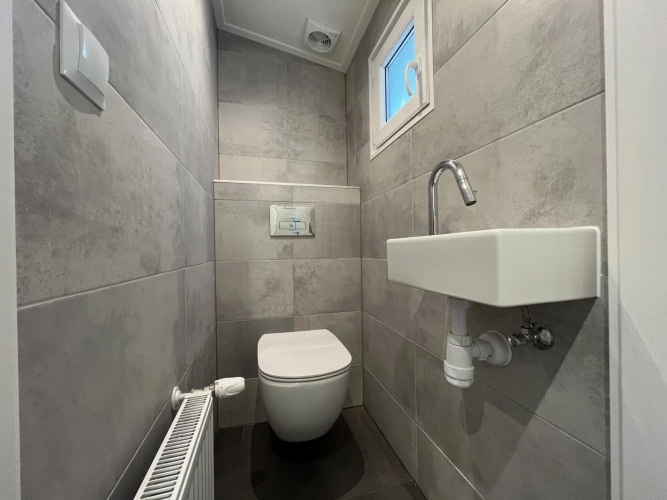 Modernes Glamping-Bad mit Wandtoilette, kleinem Waschbecken, Heizung und Fenster für Licht.