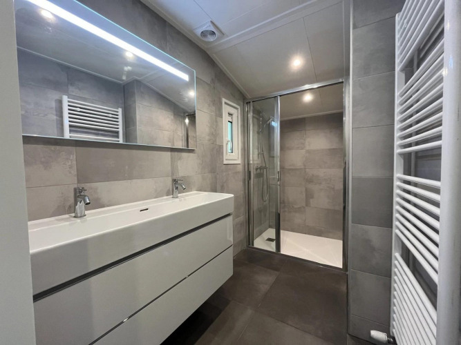 Modernes Badezimmer mit Doppelwaschbecken, großer Spiegel, Dusche und Handtuchheizung im Glamping.