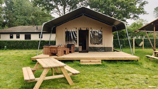 Safaritent lodge met houten veranda, picknicktafel en groene omgeving, perfect voor glamping.