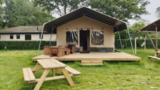 Safari-telt lodge med træterrasse, bordbænkesæt og grønne omgivelser, ideel til glamping.