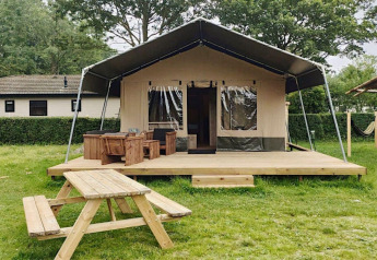 Safari-telt lodge med træterrasse, bordbænkesæt og grønne omgivelser, ideel til glamping.