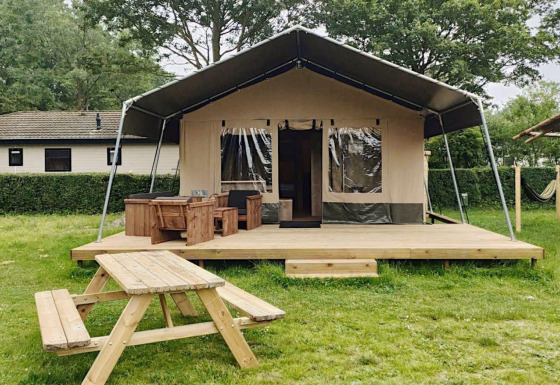 Safari-telt lodge med træterrasse, bordbænkesæt og grønne omgivelser, ideel til glamping.