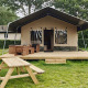 Safari-telt lodge med træterrasse, bordbænkesæt og grønne omgivelser, ideel til glamping.