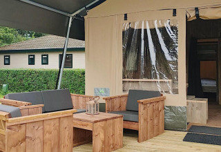 Zona de estar exterior de una tienda safari en Molengroet, Países Bajos, con muebles de madera visibles.