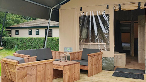 Outdoor seating area of a safari tent lodge at Molengroet in the Netherlands, showing wooden furniture.
