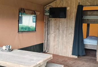 Safari tent interior at Molengroet in the Netherlands, showing wooden table, TV, and bunk beds in room.