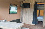 Interior de tienda safari en Molengroet, Países Bajos, con mesa de madera, televisor y literas visibles.