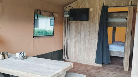 Binnenkant van Safaritent bij Molengroet in Nederland met houten tafel, tv en stapelbedden in beeld.