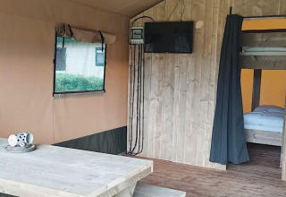 Interior de tienda safari en Molengroet, Países Bajos, con mesa de madera, televisor y literas visibles.
