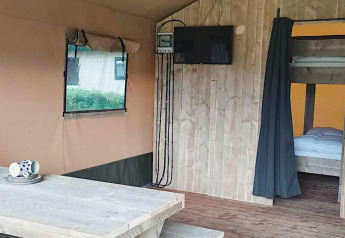 Inderside af Safari-telt ved Molengroet i Holland med bord, tv og køjesenge synlige i baggrunden.