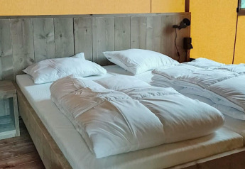 Bett in einem Safarizelt-Lodge im Molengroet in den Niederlanden mit Holzwand und weißer Bettwäsche.