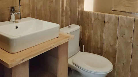 Badezimmer mit weißem Waschbecken und Toilette, umgeben von Holzvertäfelung im Safari-Zelt Molengroet, Niederlande.