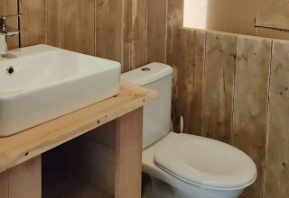 Baño con lavabo blanco y aseo, rodeado de paneles de madera, en Safari tent Molengroet en los Países Bajos.