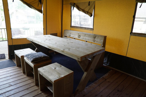 Dining area with rustic wooden table and benches inside a safari tent at Molengroet lodge in the Netherlands.