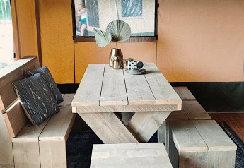 Træmøbleret spisebord med bænk og puder i en safariteltslodge ved Molengroet i Nederlandene.