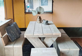 Mesa de comedor de madera con bancos y cojines en una tienda safari en Molengroet, Países Bajos.