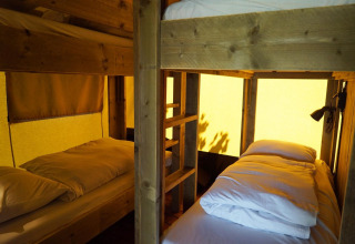 Interior de una tienda safari en Molengroet, Países Bajos, con literas de madera y ropa de cama cómoda.
