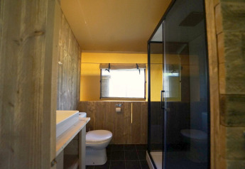Bathroom with wooden walls, modern sink, toilet, window and shower cabin inside Safari tent at Molengroet.
