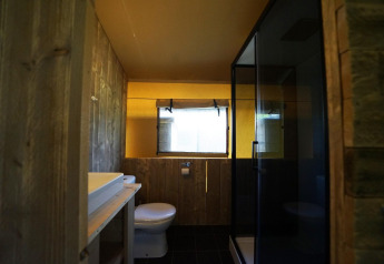 Badeværelse med trævægge, moderne håndvask, toilet, vindue og brusekabine i Safari-telt Molengroet.