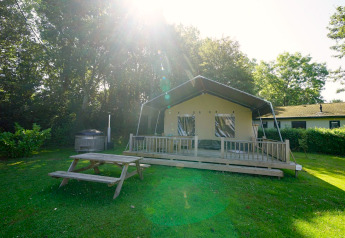Safari tent lodge at Molengroet in the Netherlands, with wooden deck, picnic table, and lush greenery.