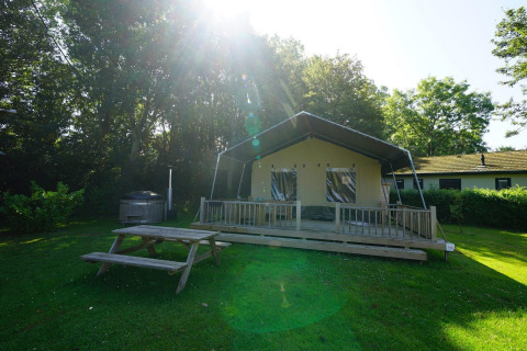 Safari-Zelt-Lodge bei Molengroet in den Niederlanden, mit Holzveranda, Picknicktisch und viel Grün.