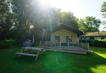 Safari-Zelt-Lodge bei Molengroet in den Niederlanden, mit Holzveranda, Picknicktisch und viel Grün.