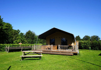 Safari tent at Molengroet in the Netherlands with a wooden deck and picnic table on grassy lawn.