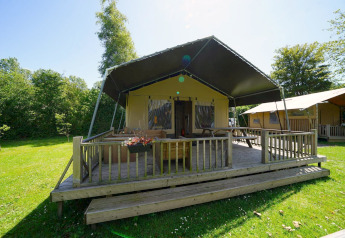 Safari tent lodge at Molengroet, Netherlands, with wooden deck, green grass, and trees under sunny skies.