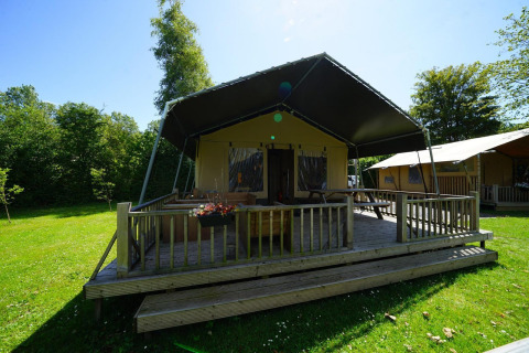 Safari-Zelt-Lodge bei Molengroet in den Niederlanden mit Veranda, grünem Rasen und Bäumen im Sonnenlicht.