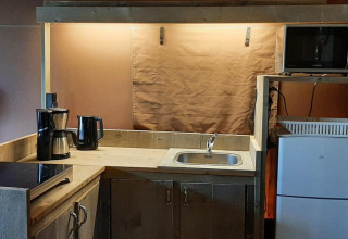 Pequeña cocina en Glampingtent Country con placa, cafetera, microondas y frigorífico visible en la imagen.