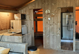 Vista interna di Glampingtent Country a Molengroet, Paesi Bassi, con cucina, letti a castello e doccia.