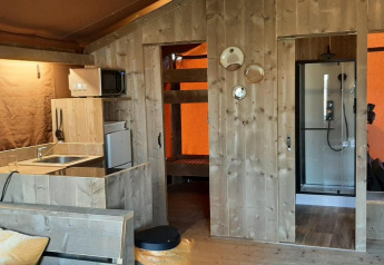 Indvendig udsigt over Glampingtent Country ved Molengroet, Holland, med køkken, køjeseng og bruser.