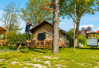 Man rides a zipline in front of a lodge on a sunny day, with green trees and grass all around the campsite.