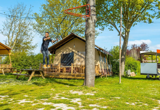 Hombre monta en tirolesa frente a una cabaña en un día soleado, rodeado de árboles y césped verde.