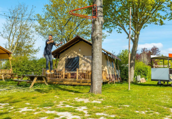Homme sur une tyrolienne devant un lodge par une journée ensoleillée, entouré d’arbres et de pelouse verte.