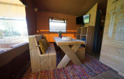 Interior de Glampingtent Desert en Molengroet, Países Bajos, con mesa de comedor de madera y alfombra colorida.