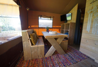 Interior de Glampingtent Desert en Molengroet, Países Bajos, con mesa de comedor de madera y alfombra colorida.