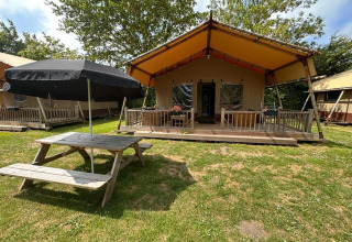 Glampingtent Desert en Molengroet, Países Bajos, con porche, mesa de picnic y sombrilla negra.