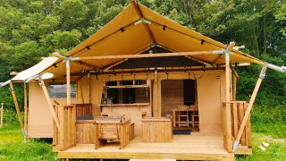 Glampingtent Dreamer lodge with wooden porch, outdoor seating, and surrounded by lush green trees.