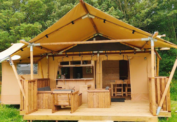 Glampingtent Dreamer con veranda in legno, area relax all'aperto e circondata da alberi verdi.
