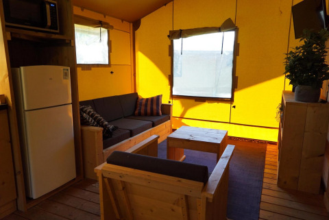 Vista interior de Glampingtent Dreamer en Molengroet, Países Bajos, con sofá, nevera y muebles de madera.