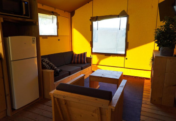 Vista interna di Glampingtent Dreamer a Molengroet nei Paesi Bassi con divano, frigo e mobili in legno.