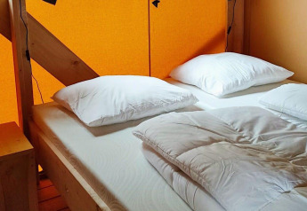 Letto accogliente con cuscini bianchi e piumone in tenda glamping al Molengroet, Paesi Bassi, con pareti arancioni.