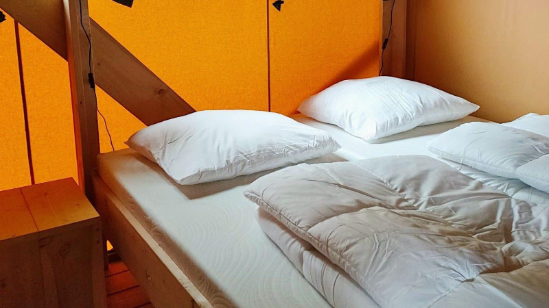 Cama acogedora con almohadas y edredón blancos en una tienda Glamping en Molengroet, Países Bajos, con paredes naranjas.
