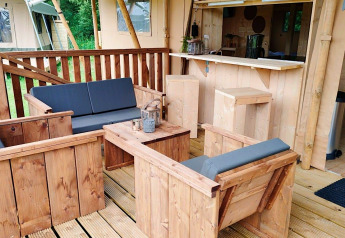 Buiten zithoek met houten meubilair en grijze kussens bij Glampingtent Dreamer, Molengroet, Nederland.