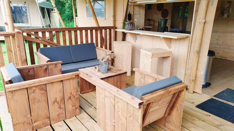 Udendørs loungeområde med træmøbler og grå hynder ved Glampingtent Dreamer, Molengroet, Holland.