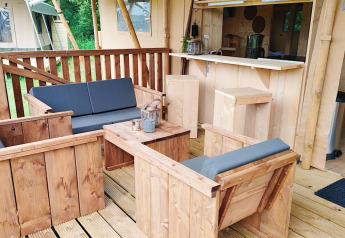 Zona de estar exterior con muebles de madera y cojines grises en Glampingtent Dreamer, Molengroet, Países Bajos.